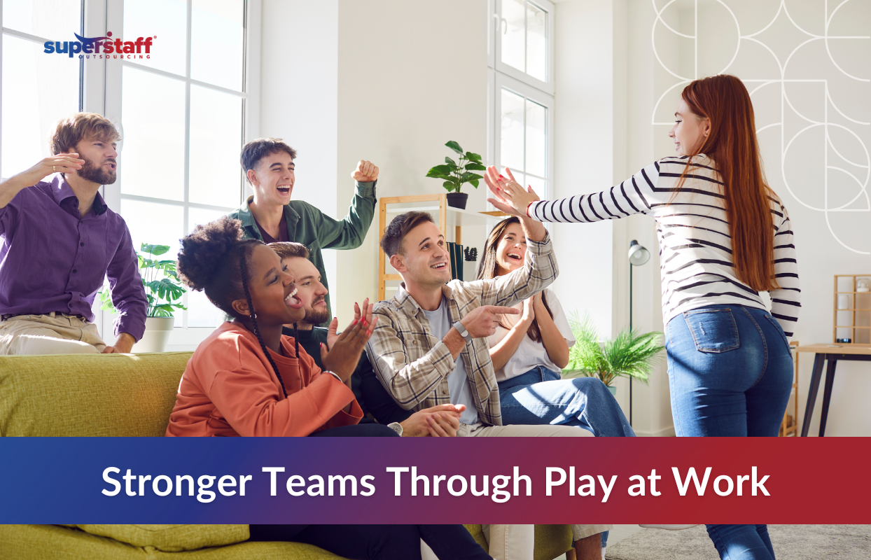 "A diverse group of young professionals engaging in a fun office game, laughing and cheering as a colleague participates. The setting is a bright, modern workplace with natural light and indoor plants, creating a relaxed and engaging atmosphere. The SuperStaff Outsourcing logo is in the upper left corner. The text overlay reads, 'Stronger Teams Through Play at Work,' emphasizing the benefits of gamifying work to enhance teamwork, motivation, and productivity in a BPO environment.